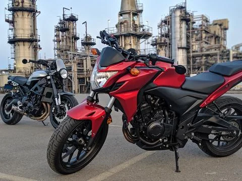 Two Motorcycles Parked in Front of Rusty Industrial Refinery Chimney at Dusk Stock-Fotos