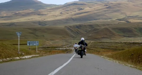 Two motorcycles ride on the road in the mountains. Motorcyclists pass by the Stock Footage 239339959