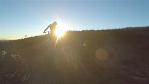 Two mountain bikers go over large jump and block out sun , drone aerial 4K Stock Footage 101110719