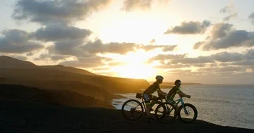 Two mountain bikers ride up to the Ocean at sunset and look out. Vídeo Stock 85527898