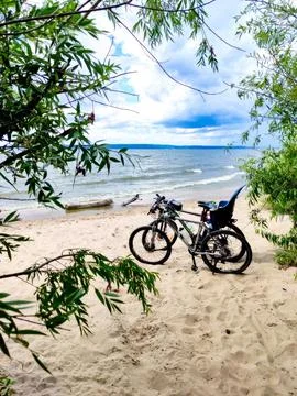 Two mountain bikes on a sandy beach. Blue sky, white clouds and green trees. Stock-Fotos
