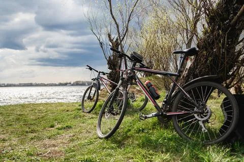 Two mountain bikes stand on the river bank. Atmospheric dynamic light. Picnic Stock Photos