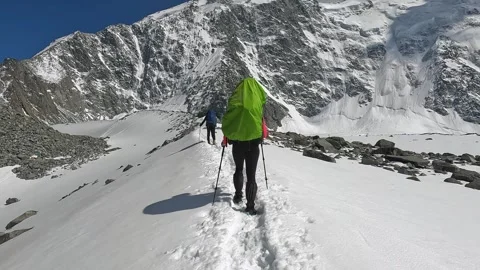 Two mountain climbers with large backpacks are walking along a snowy trail Stock-Footage 246292284