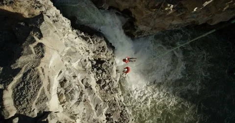 Two mountain climbers on ropes spinning over a waterfall in a deep cabin Stock Footage 64337487