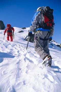 Two mountain climbers walking up snowy mountain (selective focus) Stock Photos