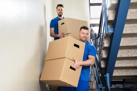 Two Movers Carrying Cardboard Boxes On Staircase Foto stock