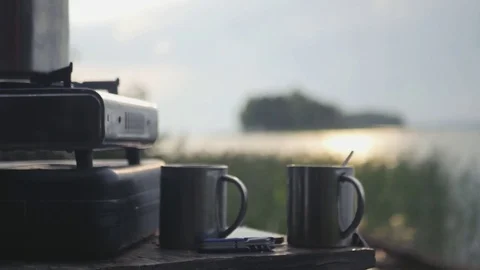 Two mugs of hot tea at a gas tourist plate against the backdrop of a lake with Stock Footage 80225529