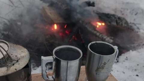Two mugs of tea stand on a log against the background of a winter fire. Stock Footage 83538061