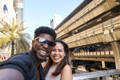 Two multethic smiling friends embracing while taking a selfie outdoors Stock Photos