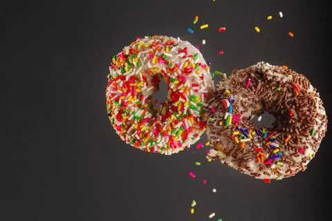Two multi-colored donuts decorated with icing sugar and confectionery sprinkl Stock Photos