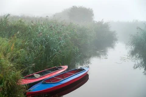 Two multi-colored kayaks on the river bank in the morning fog among the river Foto stock