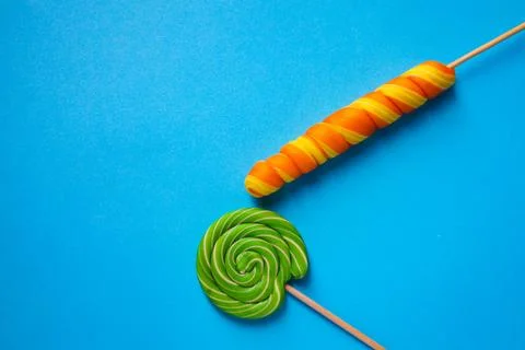 Two multi-colored lollipops of different shapes on a blue background. Space copy Stock Photos