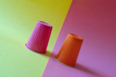 Two multi-colored plastic cups tilted on a yellow and pink background. Concept 写真素材