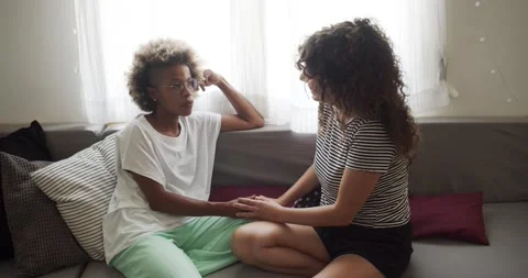 Two multi-ethnic lesbian girlfriends talking affectionately on the sofa at home. Stock Footage 162186390