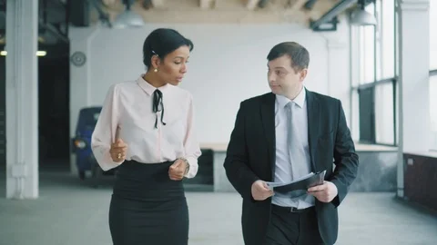 Two multi-ethnic managers, a woman and a man walk in the office and discuss the Stock Footage 107401645