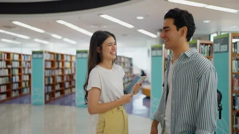 Two multi-ethnic university students standing and talking together in a library. Stock Footage 326640639