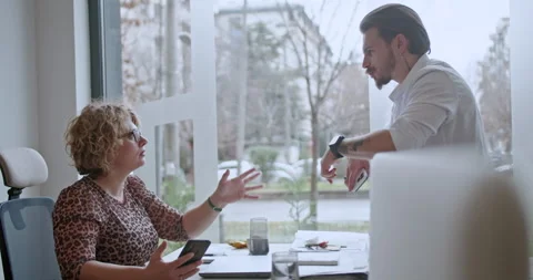 Two multi generational business employees engaging in a discussion at a well-lit Stock Footage 271150493