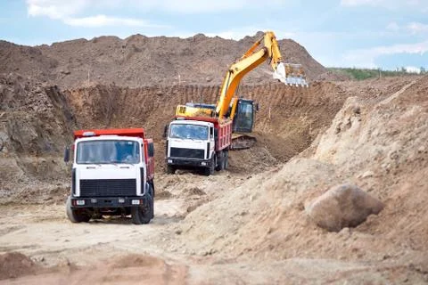 Two multi-ton mining trucks in process of loading ore by orange excavator for Stock Photos