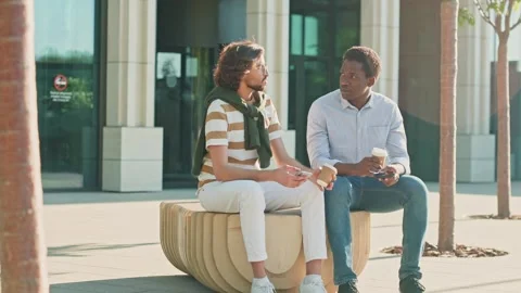 Two multicultural men sitting at park bench. Agency workers drinking coffee near Video stock 278910893