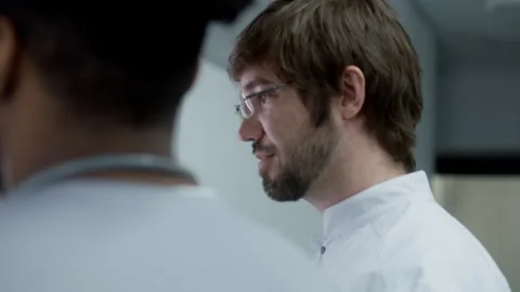 Two multiethnic doctors stand in clinic corridor and talk about work Stock Footage 249792403