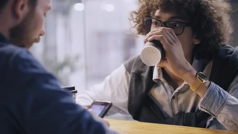 Two multiethnic friends having break sitting in cafe at table drinking coffee Stock Footage 94086288