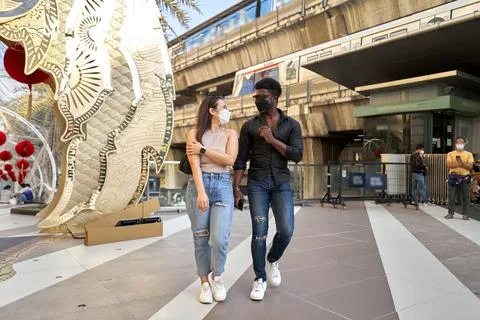 Two multiethnic friends walking through shopping mall while wearinf mask Stock Photos