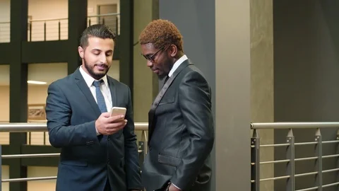 Two multiethnic managers standing in the corridor with mobile phone Stock Footage 100903754