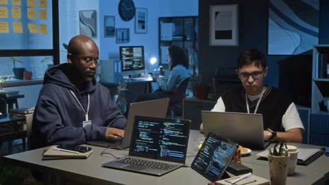 Two Multiethnic Young Male Data Analysts Working on Laptops in Dimly Lit Office Stock Footage 329615009