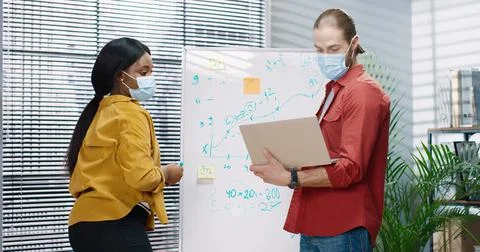 Two multinational colleagues are working on joint task at the whiteboard in Stock Photos