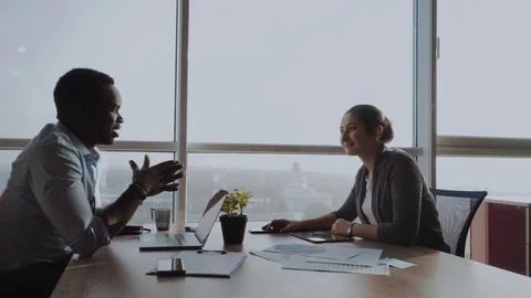 Two multinational collegues working together in an office next to a large window Stock Footage 99198106