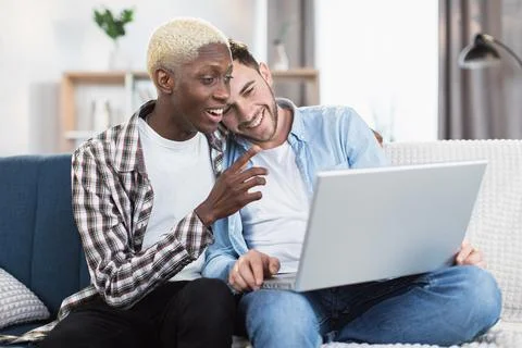 Two multiracial men in relationship using laptop on couch Stock Photos