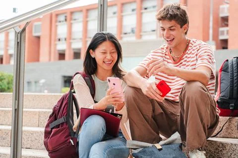 Two multiracial students sitting on a campus stairway, using a cellphone Stock Photos