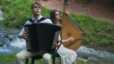 Two musicians Pianist and bandurist playing on the rocks at waterfall Stock Footage 94978053