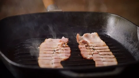 Two narrow thin pieces of bacon are being fried in a broiler pan for burger. 4K Stock Footage 82358051