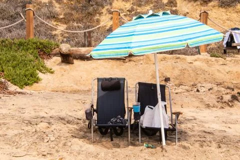 Two navy blue rusty beach chairs under a light blue striped umbrella on a bea Stock Photos