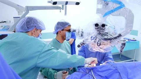 Two neurosurgeons look at microscope operating the patient.  Stock Footage 307429603