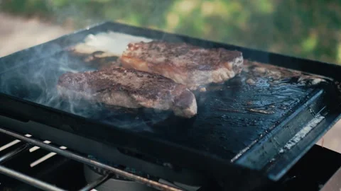 Two new york steaks searing on a flat top grill outside Stock Footage 303046345