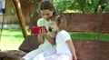 Two nice girls with red smartphone sits on the swing bench in garden HD Footage
