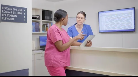 Two nurses at nurses station review patient chart on iPad, camera move right Stock Footage 109502097