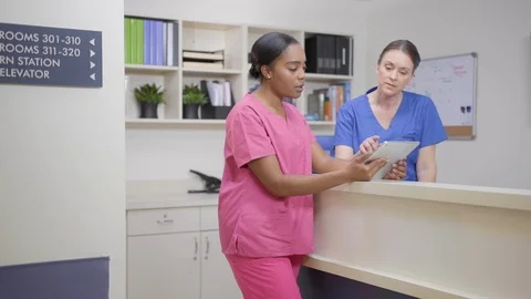 Two nurses at nurses station review patient chart on iPad, camera move left Stock Footage 109502265