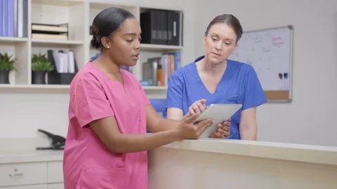 Two nurses at nurses station review patient chart on iPad, camera move left Stock Footage 109869975