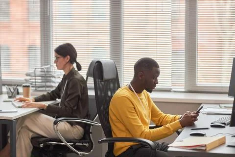 Two office workers at desks back to back working in office Stockfoto's
