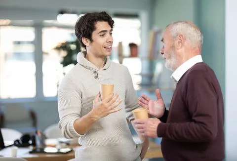 Two office workers drink coffee and chat during work break Stock Photos