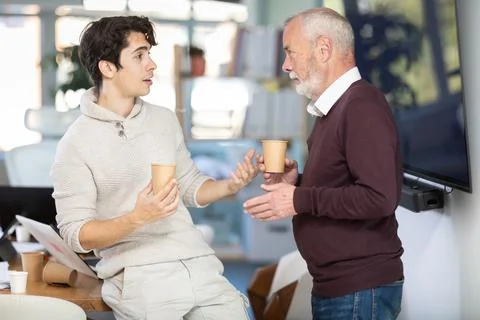 Two office workers drink coffee and chat during work break Stock Photos