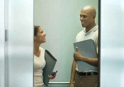 Two office workers with files talking in closing elevator Stock Photos
