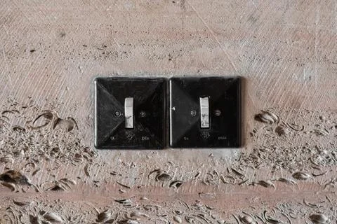 Two old black plastic square minimalist switches on a tuff-lined wall Stock Photos
