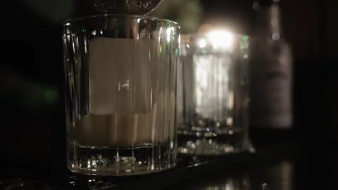 Two Old Fashioned glasses are standing on the bar counter with a cube of ice Stock Footage 240303117