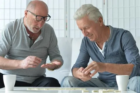 Two old men sitting at table and playing domino Stock Photos