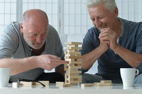 Two old men sitting at table and playing with wooden blocks Stock Photos