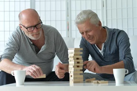 Two old men sitting at table and playing with wooden blocks Stock Photos
